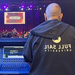 Two people's backs are facing the camera as they overlook an audio console and stage at The Plaza Live.